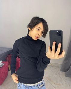 a woman taking a selfie in front of her cell phone while wearing jeans and a black sweater