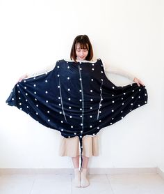 a woman standing in front of a white wall wearing a black and white polka dot blanket