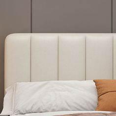 the headboard of a bed is made up with white linens and brown pillows