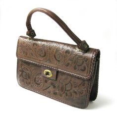 "Very nice vintage leather bag with hand-tooled designs. The bag has beautiful swirling western style design with flowers on the front, back and flap. Brass colored metal clasp. There are two interior sections divided by a zipped center section. There is also one side pocket. Measures 10.6\" x 6.5\" x 2.5\" deep. Genuine Leather, Gaitan, Made in Mexico The tooled leather sections are in wonderful shape. There are some minor scuffs from use but overall this is in very nice condition, inside and o Vintage Leather Embossed Shoulder Bag, Vintage Leather Shoulder Bag With Embossed Details, Vintage Embossed Leather Shoulder Bag, Vintage Embossed Satchel For Everyday Use, Vintage Embossed Leather Bags, Vintage Embossed Satchel Bag, Vintage Embossed Shoulder Bag For Daily Use, Vintage Hand Tooled Satchel For Daily Use, Vintage Brown Embossed Shoulder Bag