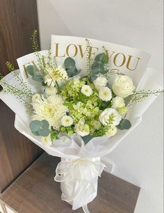 a bouquet of white flowers sitting on top of a wooden table next to a card