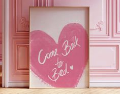 a pink heart - shaped painting with the words come back to bed written on it