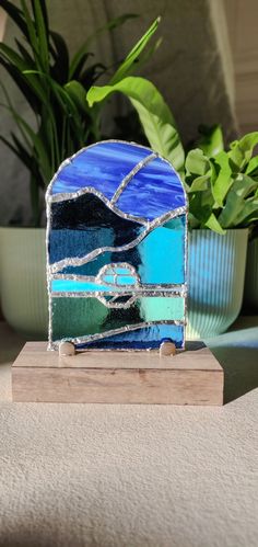 a blue and green stained glass piece sitting on top of a wooden stand next to a potted plant