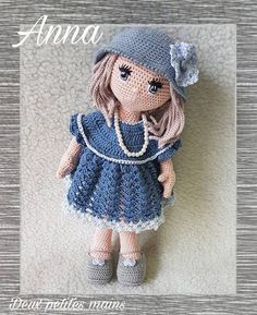 a crocheted doll wearing a blue dress and hat is posed on a white surface