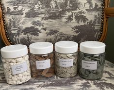 four jars filled with different types of spices on a chair in front of a tapestry