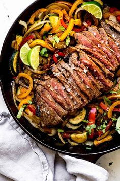 steak and vegetables in a skillet ready to be cooked with limes, peppers, onion rings, and cilantro