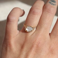 a woman's hand with a ring on it that has an oval shaped white stone in the middle