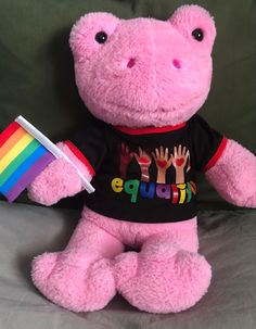 a pink stuffed animal with a rainbow cup in it's hand on a bed