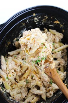 a wooden spoon in a black crock pot filled with pasta and chicken salad dressing