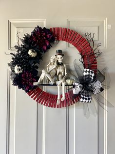 a skeleton sitting on top of a red wreath next to a black and white wreath