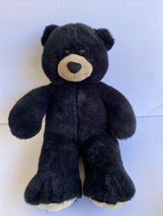 a black teddy bear sitting up against a white wall