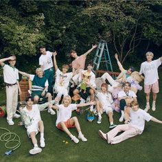 a group of people sitting and standing on top of a grass covered field next to trees