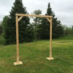 a wooden structure sitting in the middle of a grass covered field with trees behind it