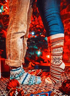 two people standing next to each other in front of a christmas tree with decorations on it