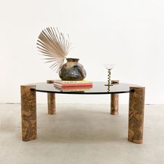 a glass table with books and a vase on top, in front of a white wall