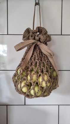 a bag filled with green apples hanging from a hook on a tiled wall in a kitchen