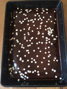 a chocolate cake with white stars on it in a black square pan sitting on a wooden table