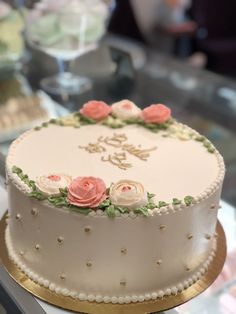 a white cake with pink flowers on it sitting on a table in front of other cakes