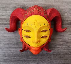 a red and yellow mask with horns on it's head sitting on a wooden surface