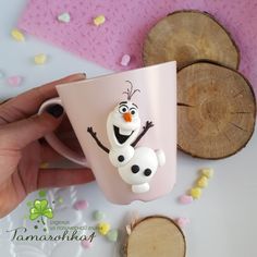 a hand holding a pink coffee mug with a cartoon character on it, surrounded by wood slices and confetti