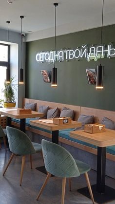 an empty restaurant with wooden tables and green chairs in front of the counter, along with neon signs on the wall