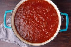 a blue pot filled with tomato sauce on top of a wooden table next to a napkin