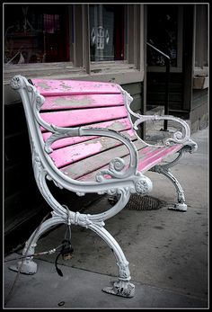 a pink and white bench sitting on the sidewalk