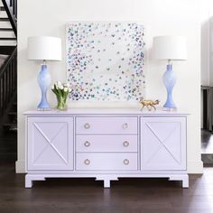 a white dresser with two lamps on top and a painting above it that says scout design studio