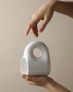 two hands holding a white ceramic object in the shape of a ball with holes on it