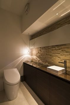 a white toilet sitting next to a sink in a bathroom under a light on the wall