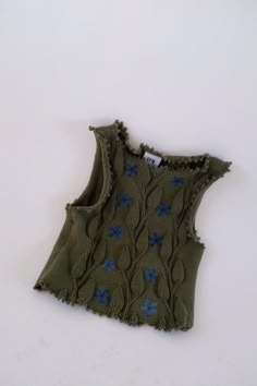 an old green sweater with blue flowers on the front and back, sitting on a white surface