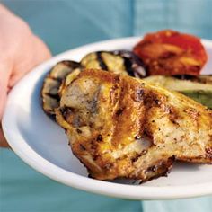 a person holding a white plate with grilled vegetables and meats on it in their hands