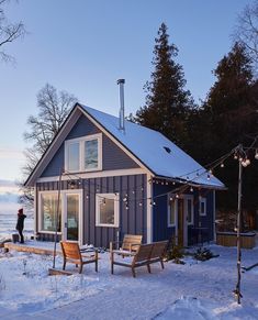 a small blue cabin in the snow with string lights