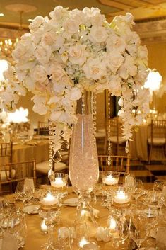 a vase filled with white flowers sitting on top of a table covered in wine glasses