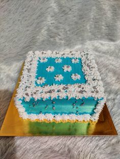 a square cake with white and blue frosting sitting on top of a gold plate