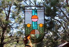 a stained glass sun catcher hanging from a pine tree in front of a window with an orange and blue design on it