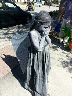 a statue of an angel talking on a cell phone while walking down the street with her hands to her face