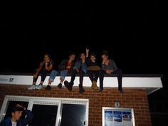 five young people sitting on top of a brick building at night with their arms in the air