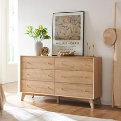 a wooden dresser sitting next to a window in a room with white walls and wood flooring