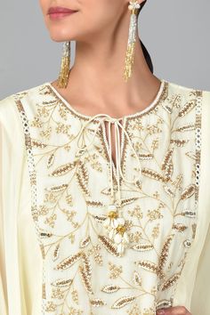 Ivory cape style tunic with zari embroidery, bugle beads and sequin work. Comes with layered sharara.
Component: 2
Pattern: Embroidered
Type Of Work: Zari, Sequin and Beads
Neckline: Round
Sleeve Type: Flared
Fabric: Georgette and Organza
Color: White
Other Details: 
Scalloped hem with shell hangings
Asymmetrical hem
Keyhole front with tie up
Occasion: Sangeet - Aza Fashions Layered Sharara, Zari Embroidery, Cape Style, Beaded Neckline, Sharara Set, Embroidered Tunic, Bugle Beads, Fashion App, Scalloped Hem