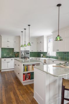 a large kitchen with white cabinets and green tile backsplash, wood flooring