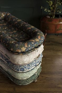 a pile of cushions sitting on top of a wooden floor next to a planter