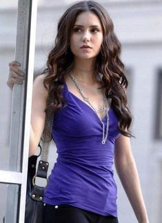 a beautiful young woman standing next to a window holding onto a handbag and looking at the camera