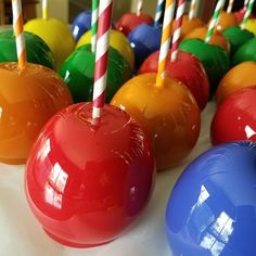 colorful candy apples are lined up on a table with striped candles in the middle and one is red, yellow, green, blue, and orange