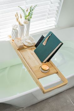 a bath tub with a wooden tray holding books and candles