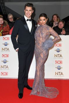 a man and woman in formal wear posing on the red carpet at an awards event