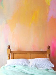 a bed sitting in front of a wall with colorful paint painted on it's walls