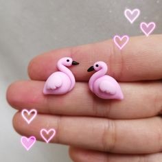 two tiny pink flamingos are sitting on someone's hand with hearts in the background