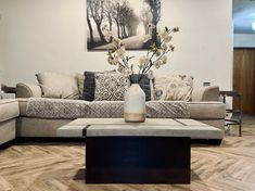 a living room filled with furniture and flowers on top of a coffee table in front of a painting