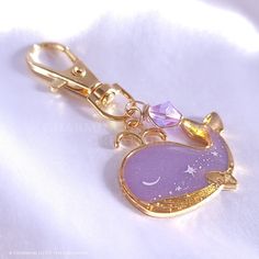 a gold key chain with a purple glass charm hanging from it's side on a white cloth